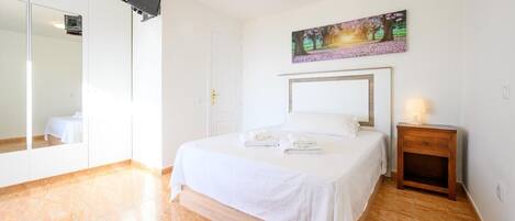 A bedroom with a bed, a bedside table with a lamp, a painting on the wall, and a large mirror.