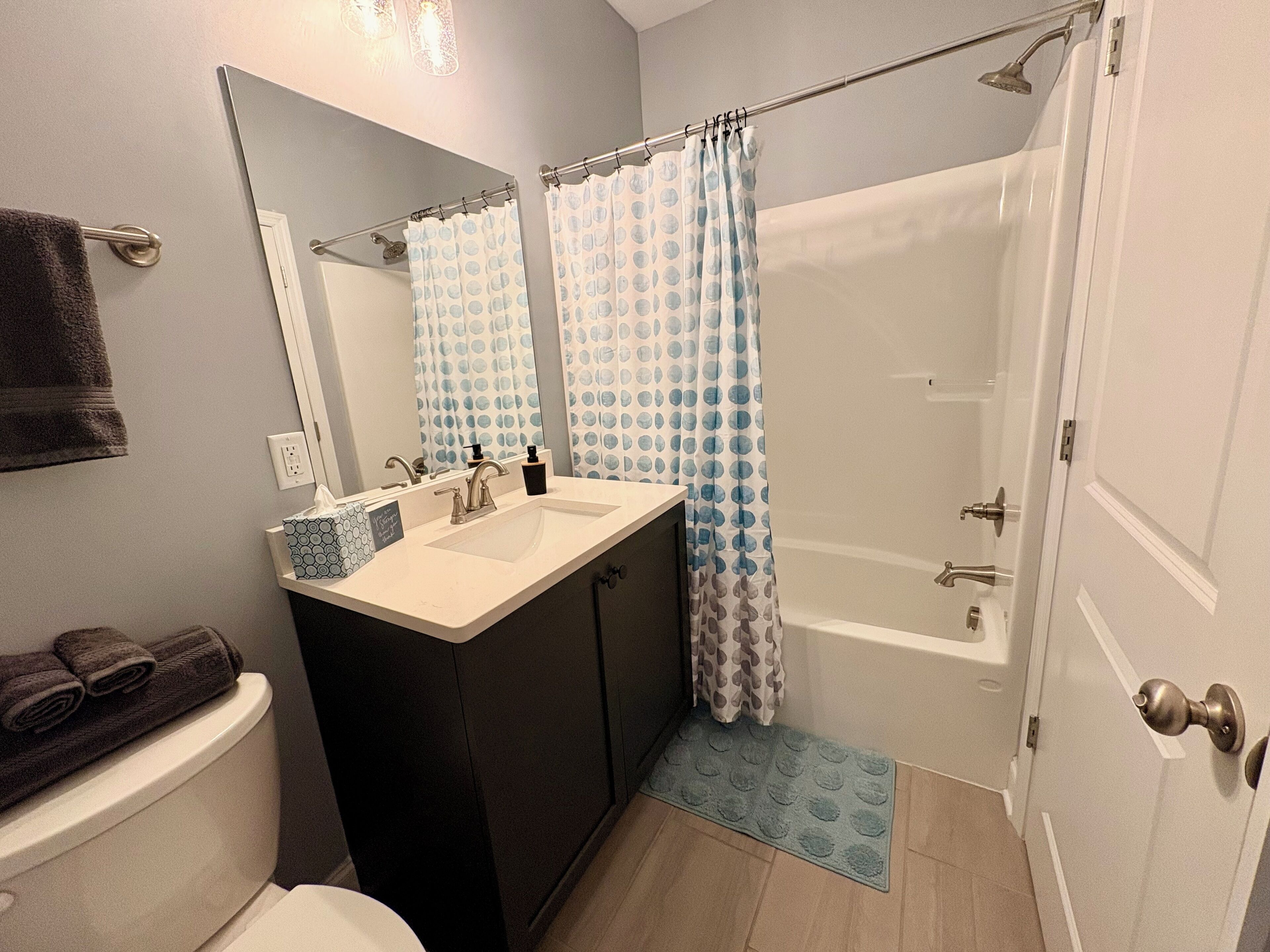 A bathroom with a sink, mirror, toilet, and shower area.