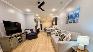 A modern living room with a flat-screen TV, a sofa, a coffee table, and a dining area in the background. - Urban Oasis 456 - Close to everything in Cleveland! (Cleveland)