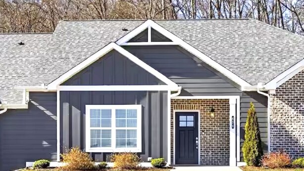 A residential house with a dark gray exterior, a white-framed garage door, and a brick section on the right side. - Urban Oasis 456 - Close to everything in Cleveland! (Cleveland)