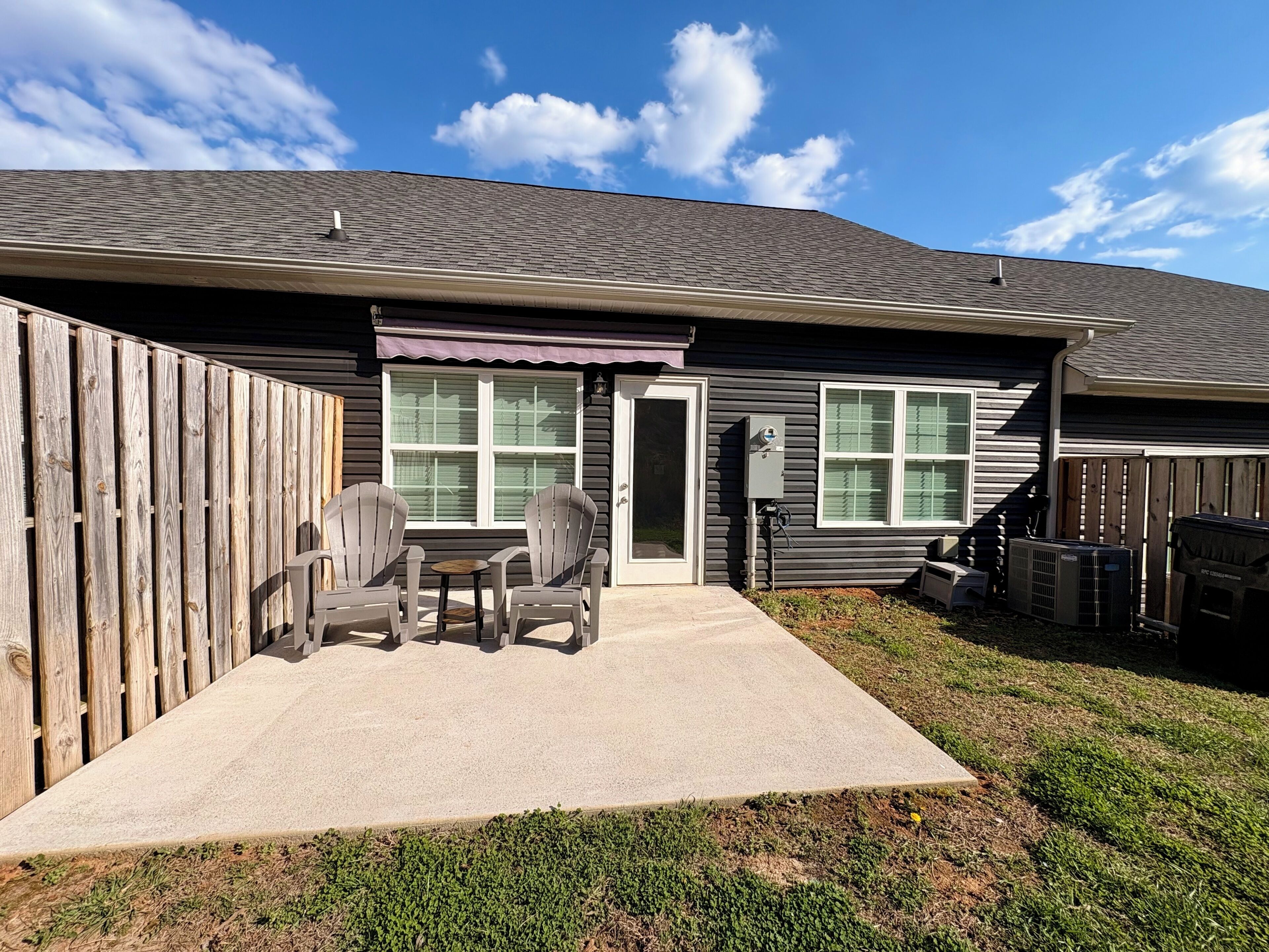 A residential house with a covered patio, two chairs, and an air conditioning unit.