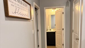 A hallway with a framed sign on the wall, wooden flooring, and a door leading to a bathroom. - Urban Oasis 456 - Close to everything in Cleveland! (Cleveland)