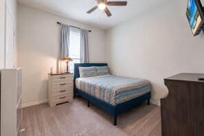 Ein Schlafzimmer mit einem Bett, einer Kommode, einem Deckenventilator und einem Fernseher an der Wand.