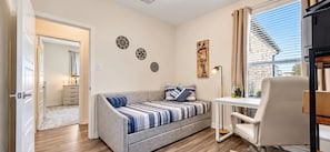 Ein modernes Wohnzimmer mit einer Couch, einem Schreibtisch und einem Sessel. An den Wänden befinden sich dekorative Kunstwerke und ein Fenster mit Vorhängen.