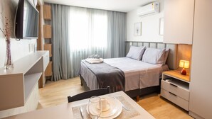 Et moderne hotelværelse med seng, sengebord, fjernsyn og et spiseområde med et bord dækket til to personer.