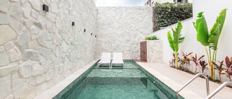 A swimming pool with stone walls and two lounge chairs.