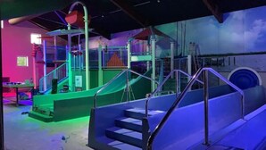Un espace de jeux intérieur, bien éclairé, avec un toboggan, des escaliers et une structure d’escalade.