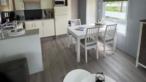 Une cuisine compacte avec des meubles blancs et un four à micro-ondes, un coin repas avec une table et des chaises blanches, et une fenêtre donnant sur un paysage verdoyant.