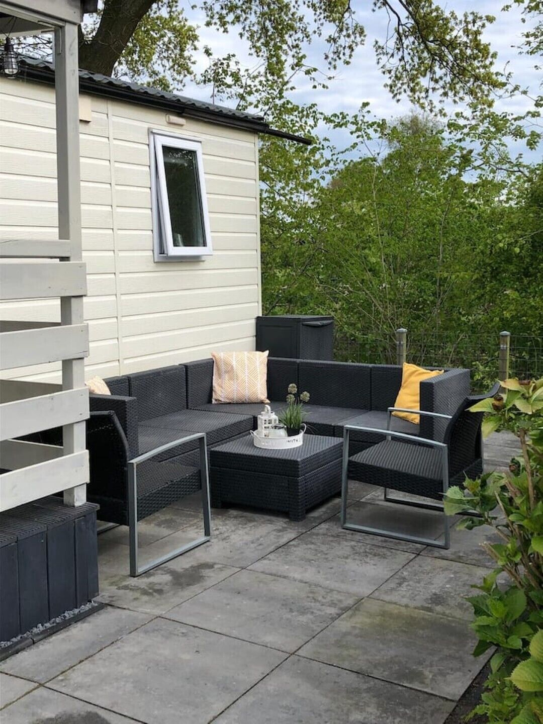 An outdoor patio area with a dark wicker sofa set, a small table with a plant, and a white trash bin.
