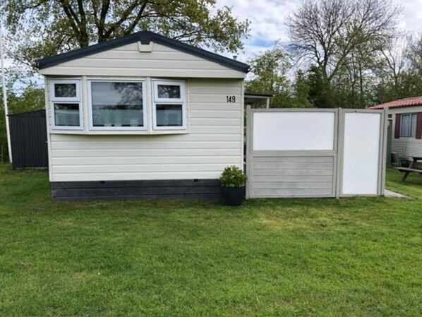 A small, single-story mobile home with a number '149' on the side, a small front porch, and a fenced yard.