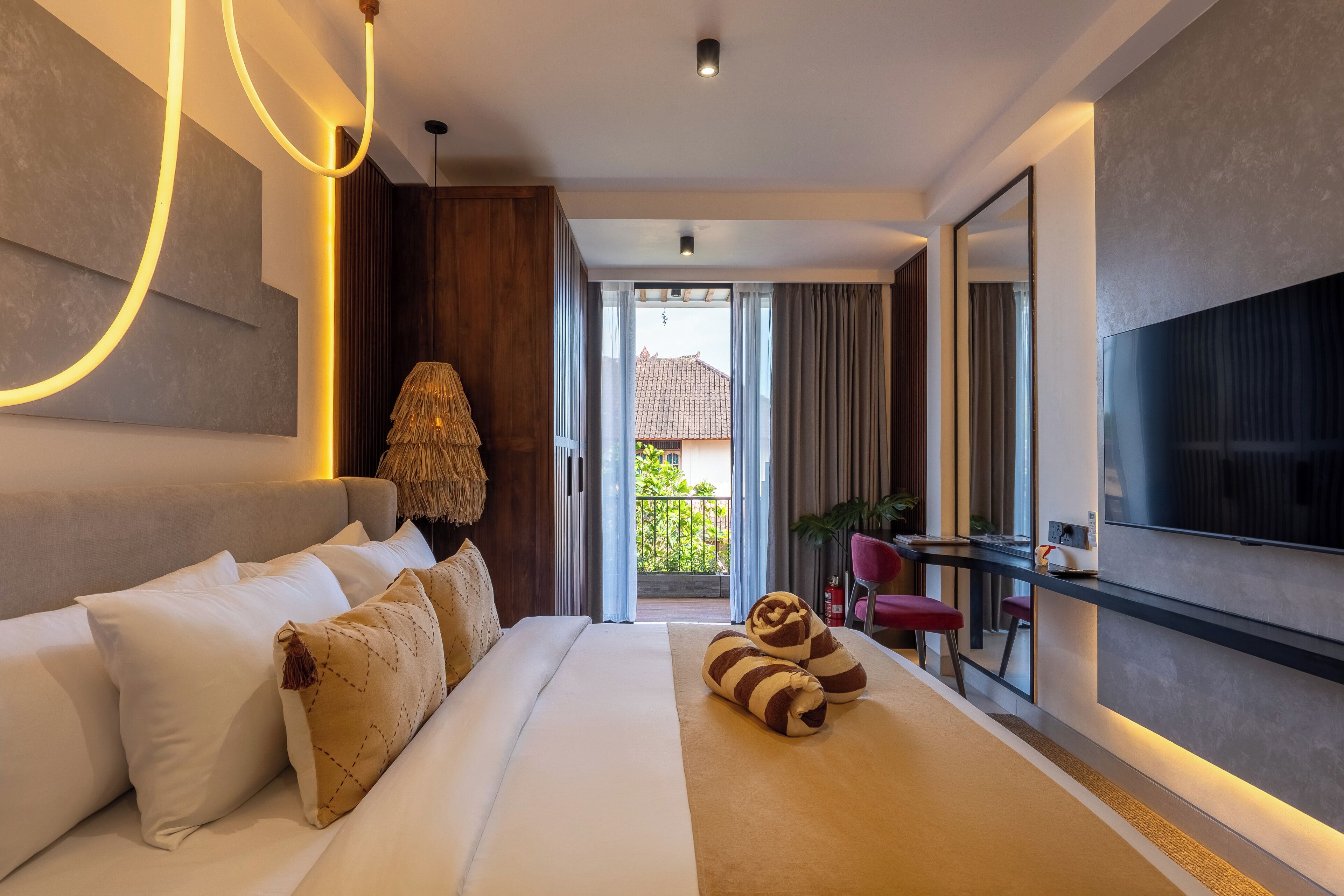 Une chambre d’hôtel moderne dotée d’un grand lit, d’une télévision et d’un balcon offrant une vue sur la verdure.