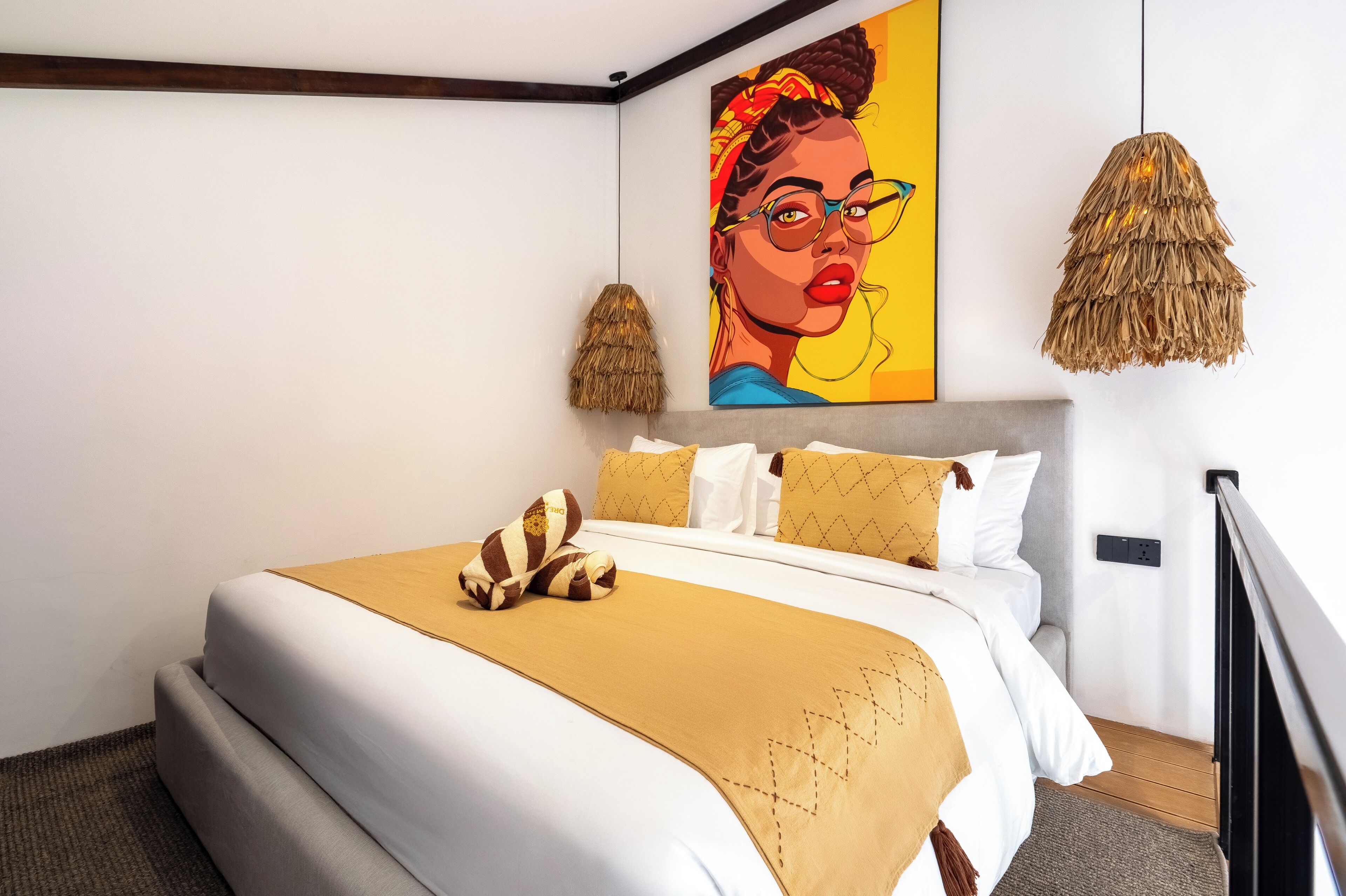A neatly made bed with a beige bedspread, two pillows, and a decorative pillow. There is a large painting on the wall above the bed.