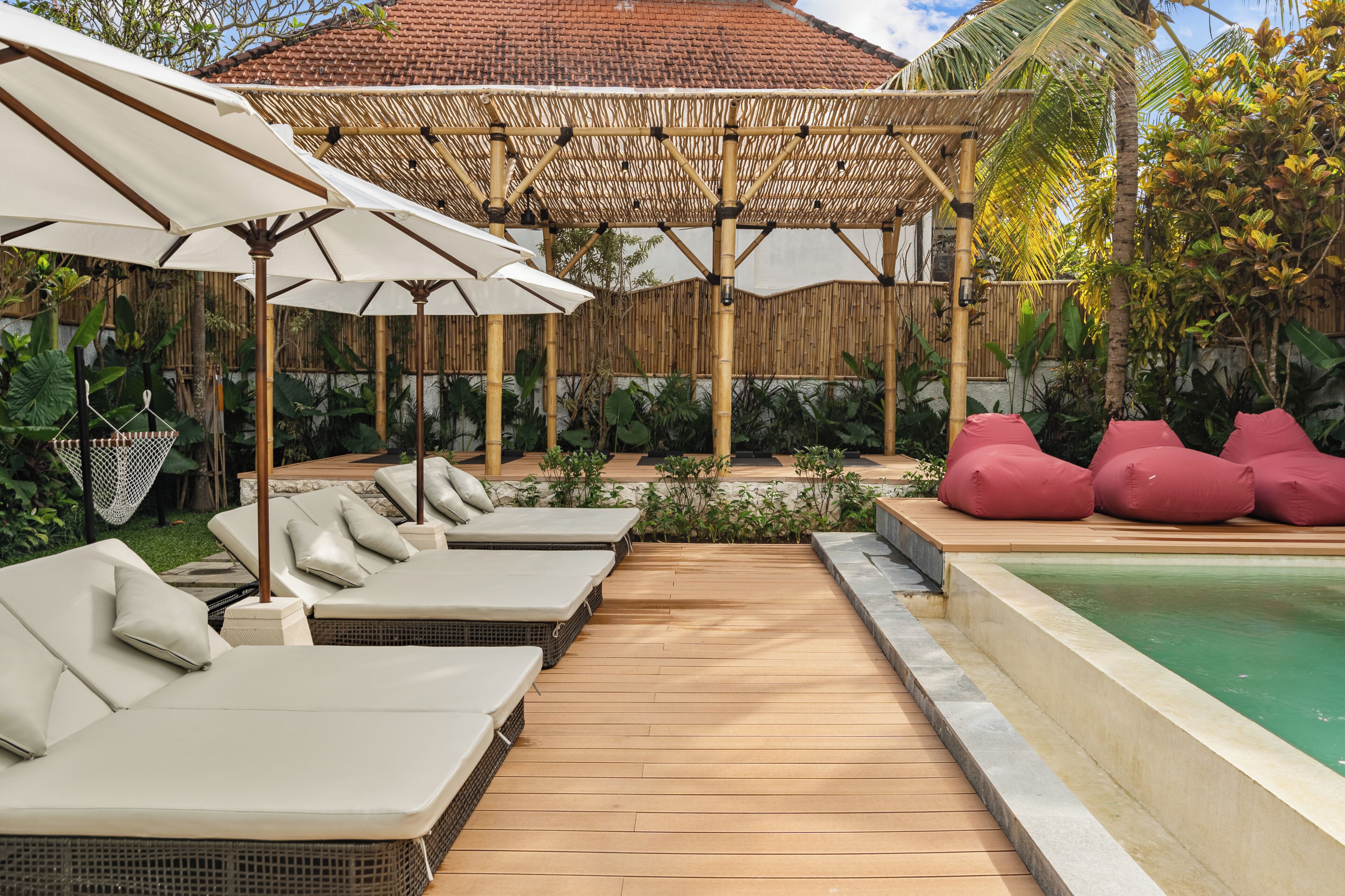 A poolside area with lounge chairs, umbrellas, and a bamboo pergola.