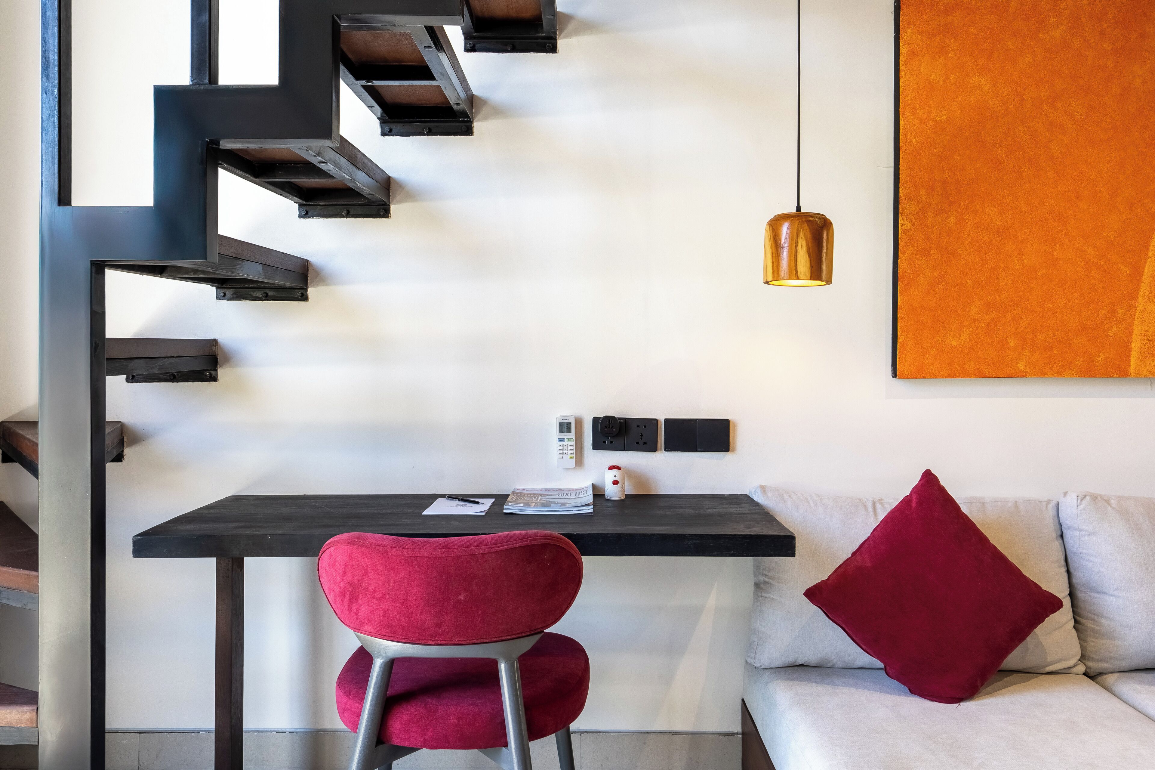 A modern interior with a staircase, a desk with a chair, a sofa, and a pendant light.