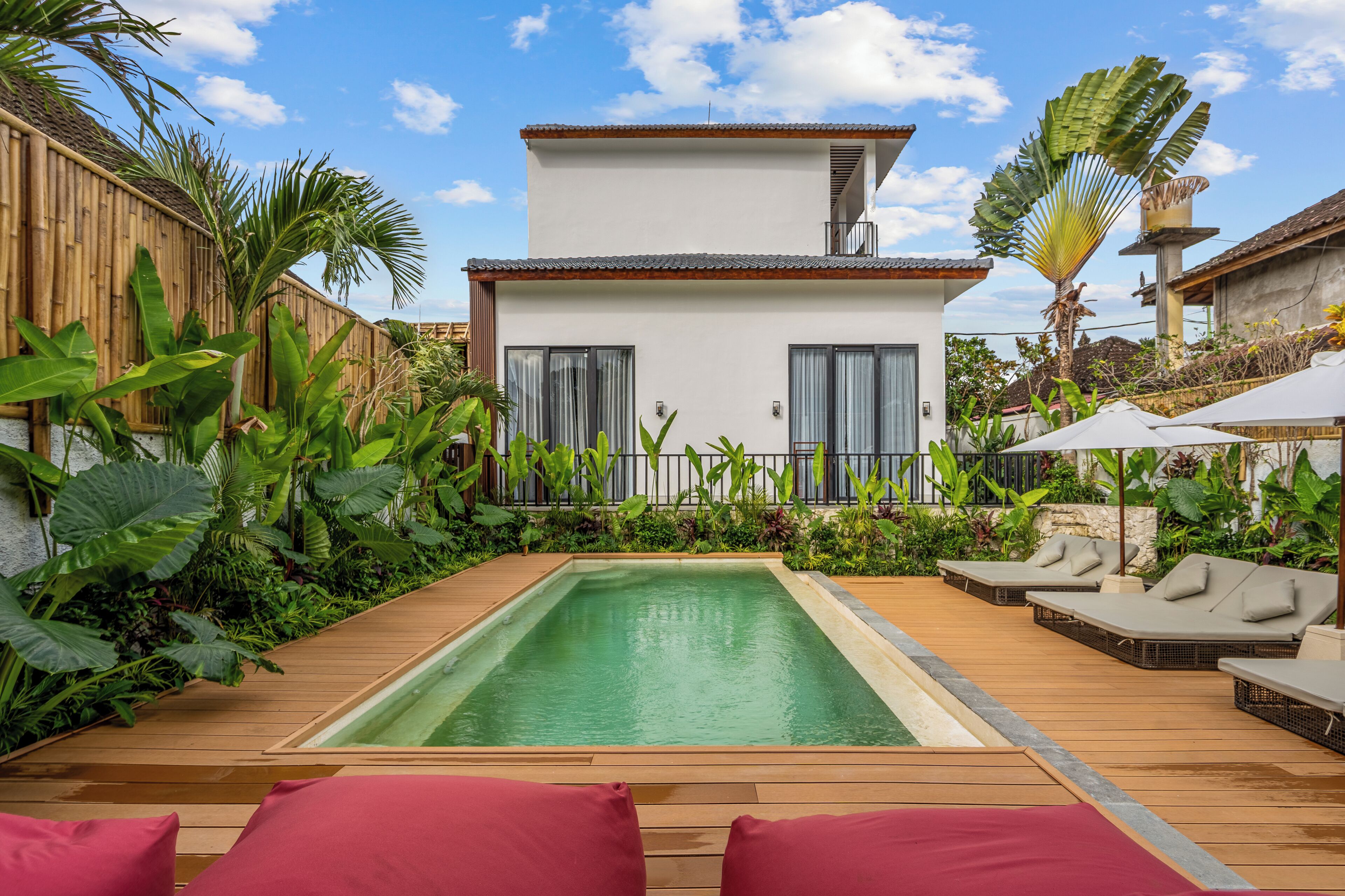 A modern house with a swimming pool, surrounded by lush greenery and a wooden deck.