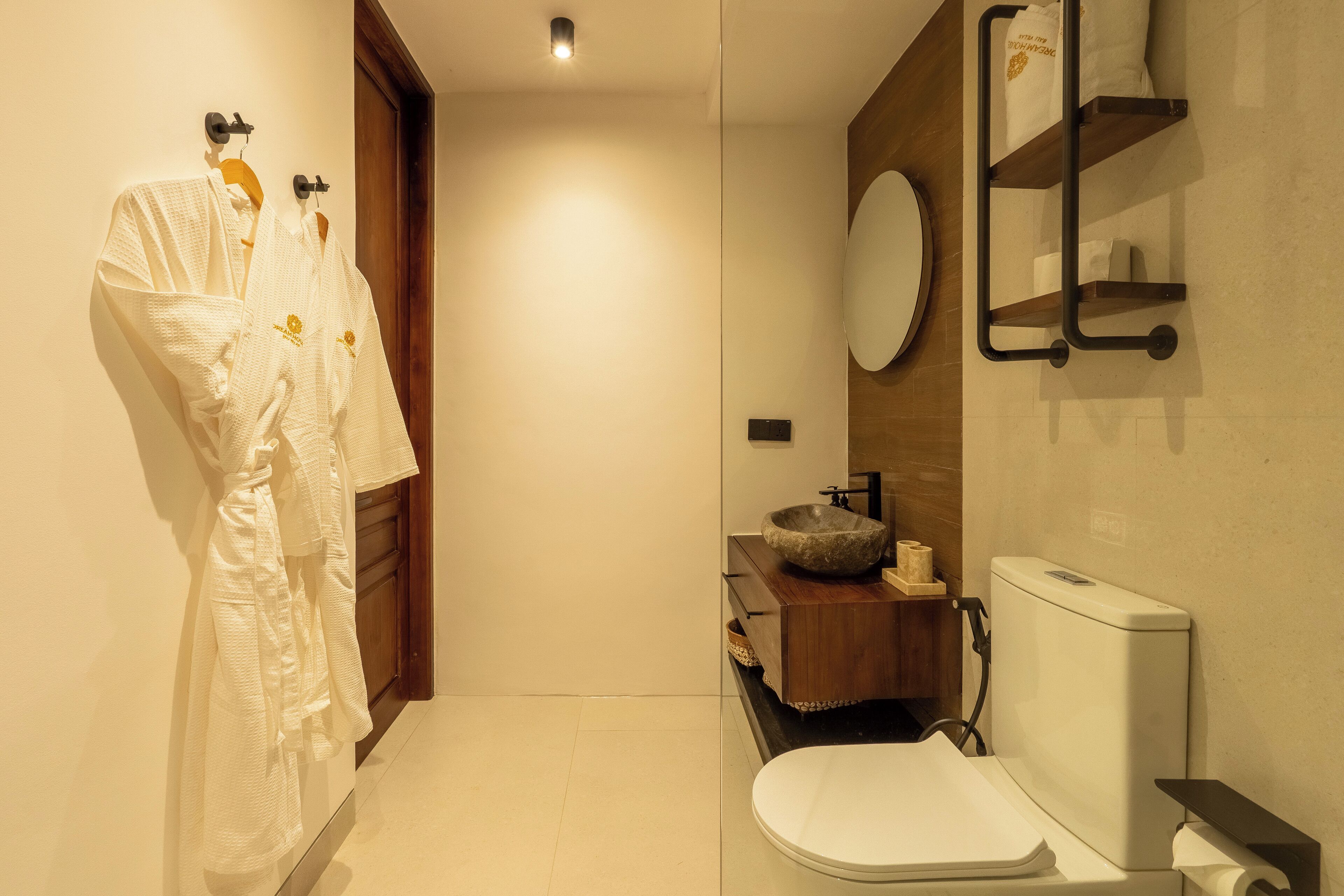 A modern bathroom with a wooden vanity, a round mirror, and a white toilet.