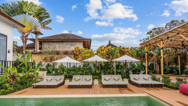 A pool area with lounge chairs and umbrellas, surrounded by lush greenery and a traditional building. - Palermo Suites by DH (Ubud)