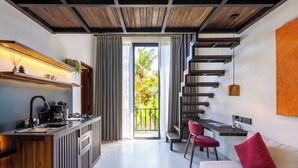 A modern kitchen with a built-in island, a dining area with a red chair, and a sofa with a red pillow. - Palermo Suites by DH (Ubud)