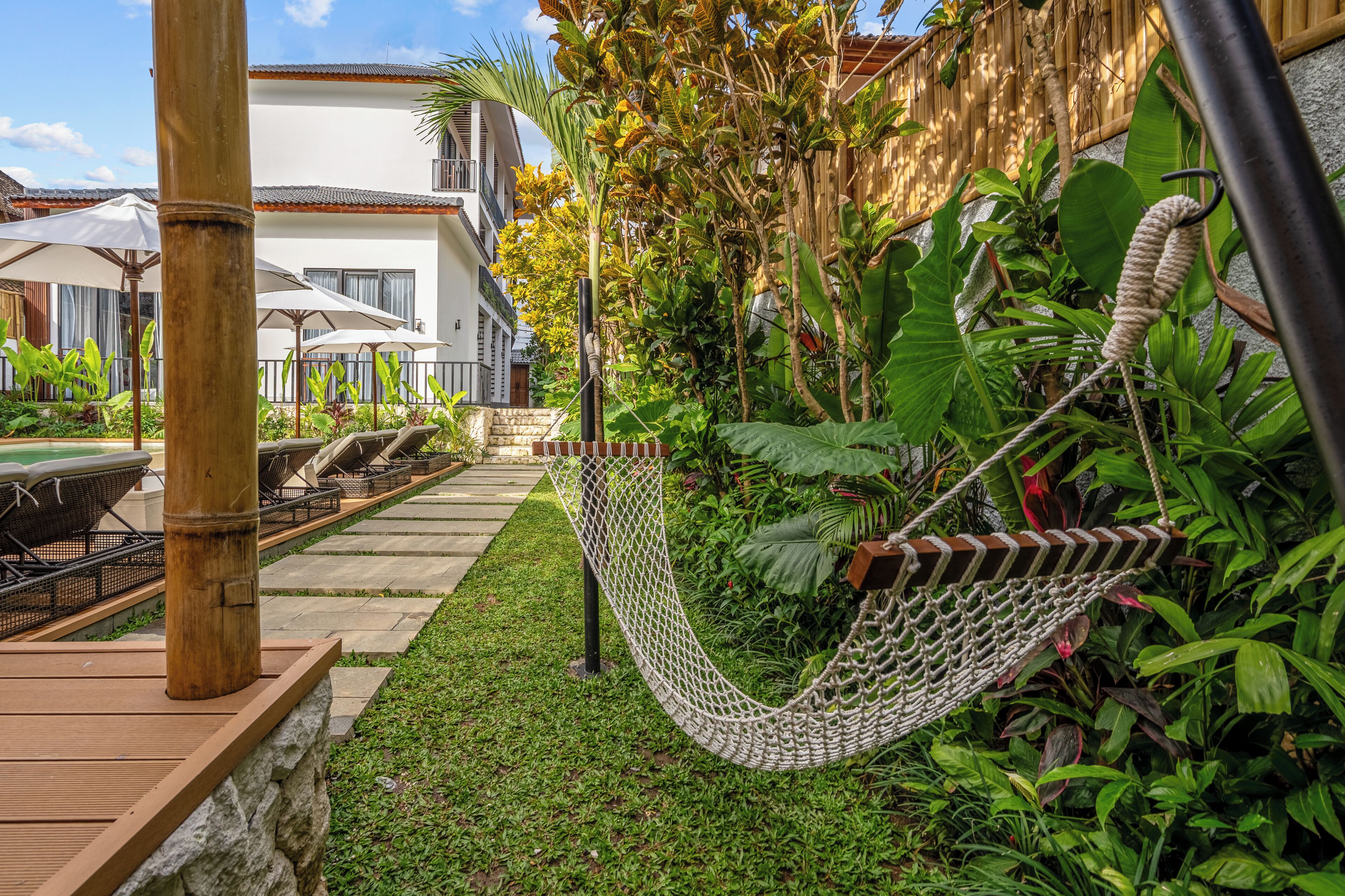 Una hamaca en un jardín exuberante con piscina y mobiliario exterior.