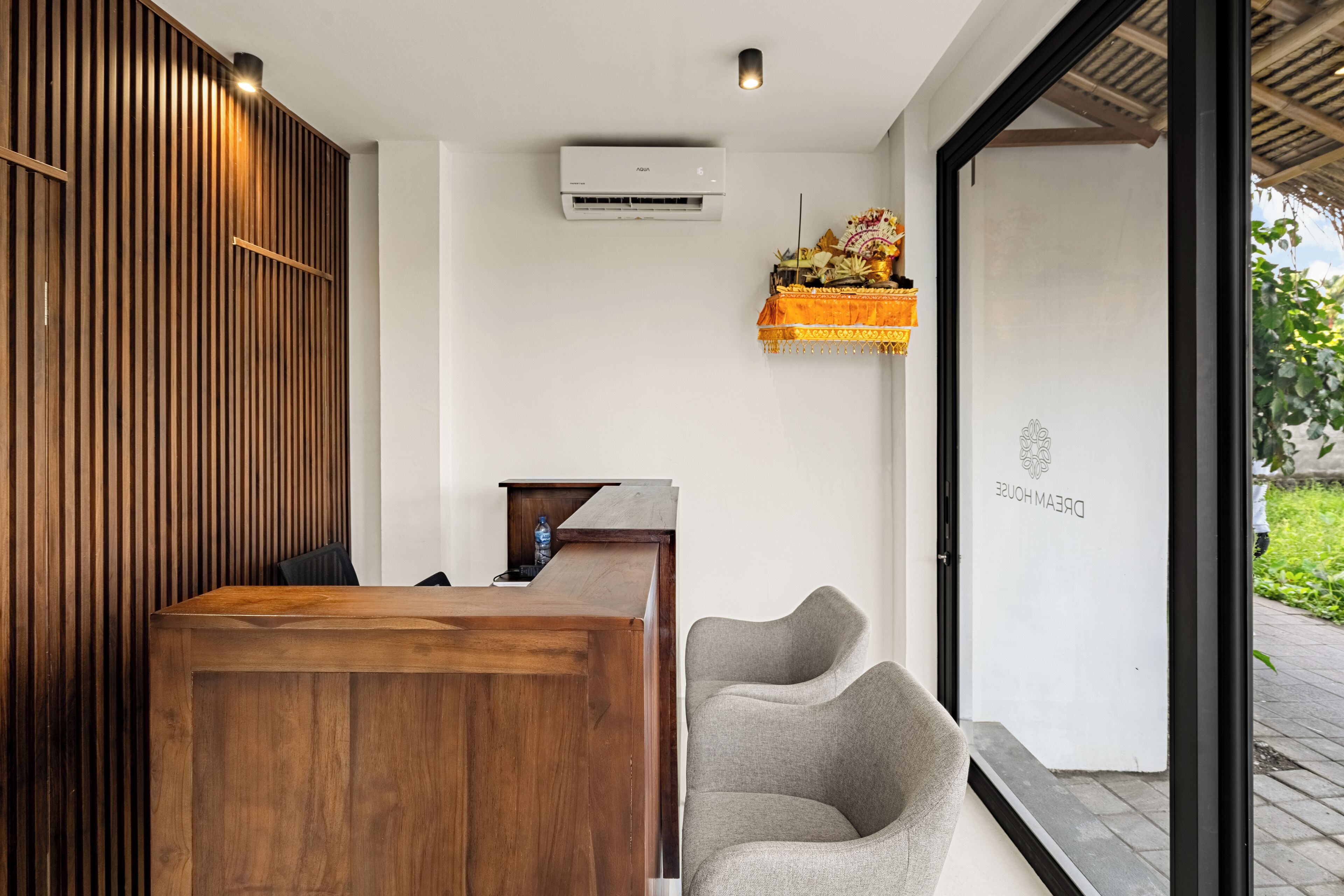 A reception desk with a wooden finish, a grey upholstered chair, and a wall-mounted air conditioner.
