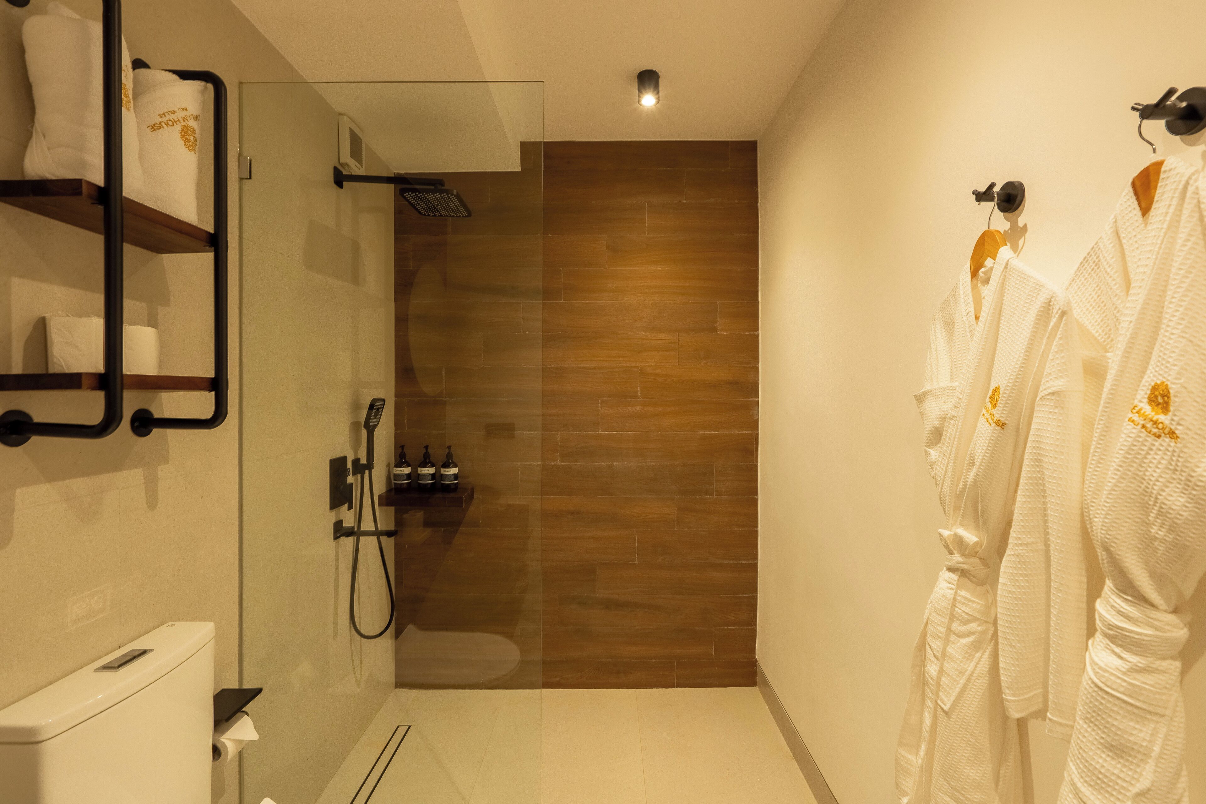 Un baño moderno con ducha envuelta en vidrio, paneles de madera en la pared y toallas blancas en un estante.