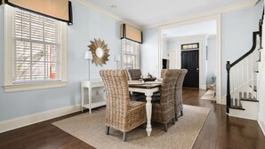 A dining area with a table and chairs, a lamp, and a large window with blinds. - Picture Perfect Charleston Living on Spring St (Charleston)