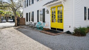 A white building with a yellow door, a brick entrance, and a gravel driveway. - Picture Perfect Charleston Living on Spring St (Charleston)