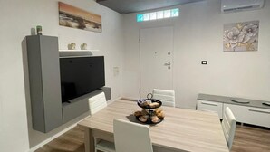 Moderni keittiö, jossa on sisäänrakennettu televisio, valkoiset tuolit ja puinen ruokapöytä.