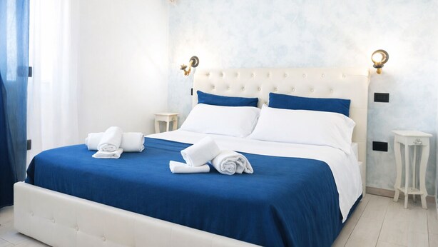 Un letto rifatto con lenzuola blu e bianche, due comodini e un lampadario fissato alla parete.