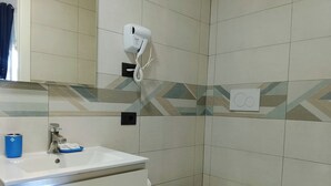 Un bagno con un lavandino bianco, un water e un bidet. È presente un asciugacapelli montato a parete. Le pareti sono rivestite di piastrelle con un motivo geometrico.