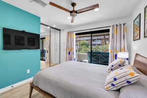 A bedroom with a bed, a ceiling fan, a TV mounted on the wall, and a balcony with curtains. - Atomic Starburst – Mountain View Downtown Condo (Palm Springs)