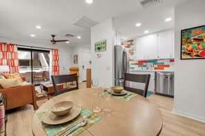 A modern kitchen with white cabinets, a stainless steel refrigerator, and a colorful backsplash. - Atomic Starburst – Mountain View Downtown Condo (Palm Springs)