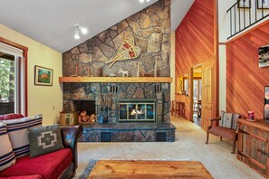 A cozy living room with a stone fireplace, wooden furniture, and a view of the outdoors. - Mountain Getaway w/ Hot Tub & Fireplace (Sisters)