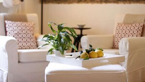 Ein modernes Wohnzimmer mit einem weißen Sofa, gemusterten Kissen, einem kleinen Tisch und einer Schale mit Zitronen und einer Topfpflanze.