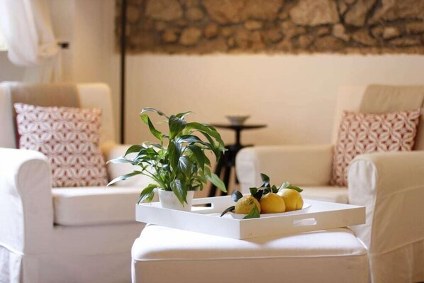 A modern living room with a white sofa, patterned cushions, a small table, and a tray with lemons and a potted plant.