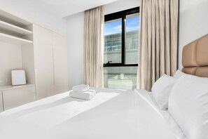 A modern hotel room with a large bed, a wardrobe, and a window with curtains. - Stayshort - Luxury 3BR Apartment in Meydan That Sleeps 5 (Dubai)