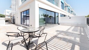 Un edificio moderno con amplios ventanales de vidrio, un patio con mesa y sillas, y fachada blanca.