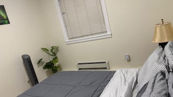 Ein Schlafzimmer mit einem Bett, einem Heizkörper, einem Fenster mit Jalousien, einer Lampe und einer Pflanze.