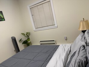 Un dormitorio con una cama, un radiador, una ventana con persianas, una lámpara y una planta.