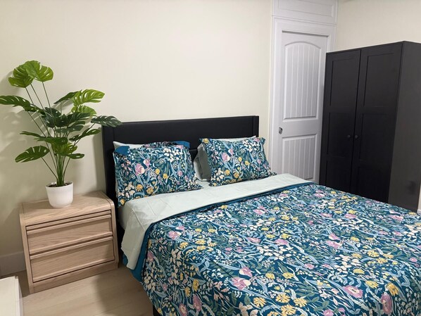A bedroom with a bed, a nightstand, a potted plant, and a wardrobe.
