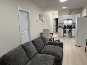 Een woonkamer met een bank, een eethoek met een tafel en stoelen, en een keuken met apparatuur.