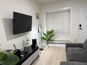 Una sala de estar con televisor de pantalla plana, un sofá, una mesa de centro y dos plantas en macetas.
