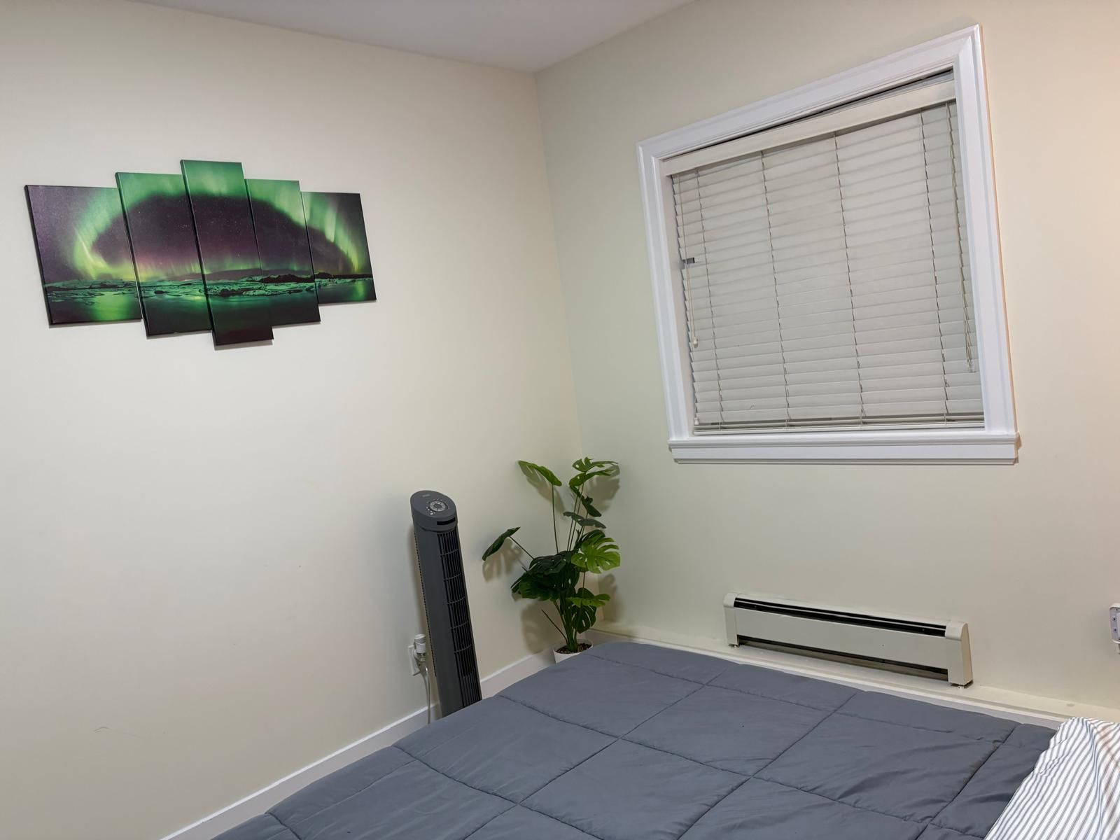 Un dormitorio con cama, radiador, ventana con persianas, aire acondicionado instalado en la pared y una obra de arte en la pared.