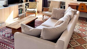 Een woonkamer met een bank, stoelen, een televisie, een boekenkast en een kamerbreed tapijt met een patroon.