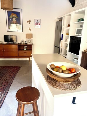 A modern kitchen with a central island, wooden bar stool, and a bowl of fruit. - WINEGROWER'S HOUSE (Escales)