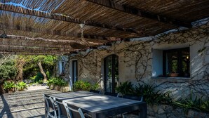 Un patio al aire libre con mesa y sillas, una pérgola y un muro de piedra con plantas.