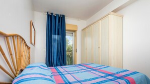 Un dormitorio con cama, una silla de madera, un armario y una ventana con cortinas.