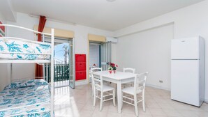 Una habitación con literas, una mesa de comedor, sillas, un refrigerador y un armario rojo.