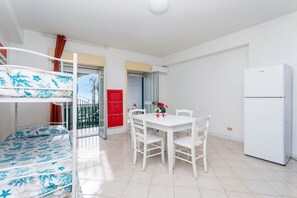 Una habitación con literas, una mesa de comedor, sillas, un refrigerador y un armario rojo.
