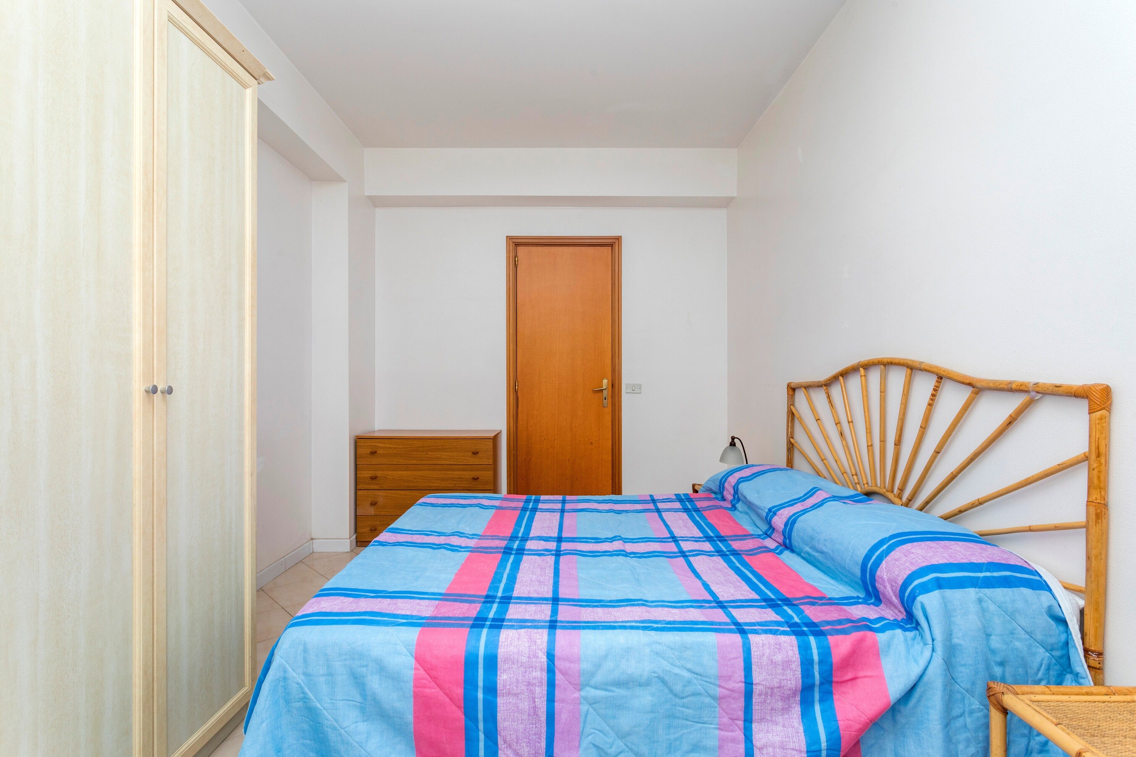 A bedroom with a bed, wooden wardrobe, and a door.